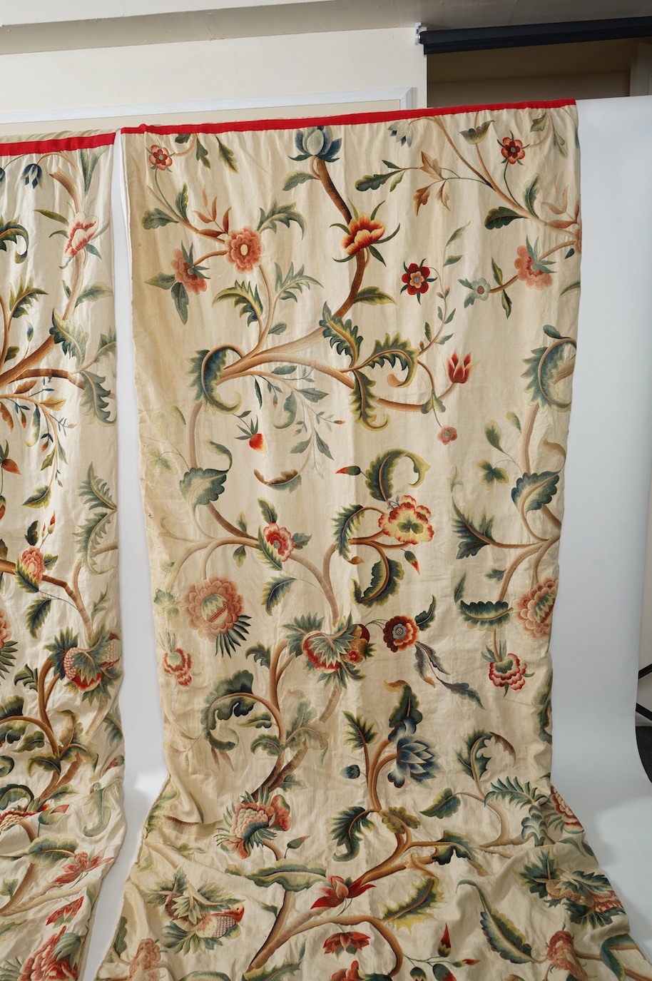 Six 20th century crewel work ‘Tree of Life’ cream linen curtains. Worked at the base in coloured wools depicting a pastoral scene of a shepherd playing a flute amongst sheep, deer, squirrels and flowers with a dog chasin